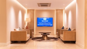 A modern reception area with a large TV screen displaying a welcome message, two sofas, a coffee table, and a lamp.