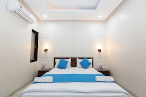 Ein Hotelzimmer mit Bett, zwei Nachttischen, einer Klimaanlage und einem Beistelltisch mit Telefon und einer Schachtel.