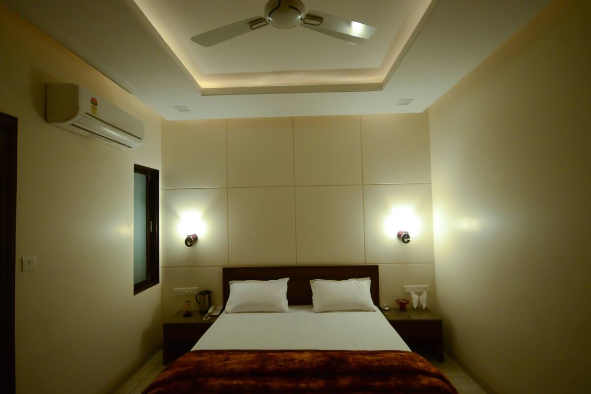 A hotel room with a bed, a ceiling fan, wall-mounted air conditioning, bedside lamps, and a nightstand.