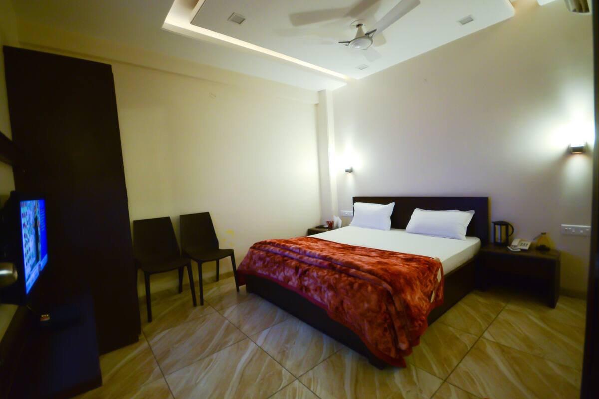 A hotel room with a bed, a TV, two chairs, a nightstand, and a ceiling fan.