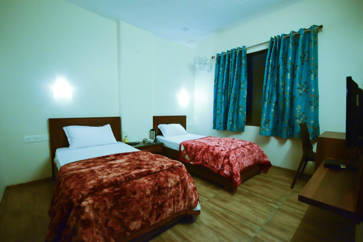 A hotel room with two beds, a desk, and a window with curtains.