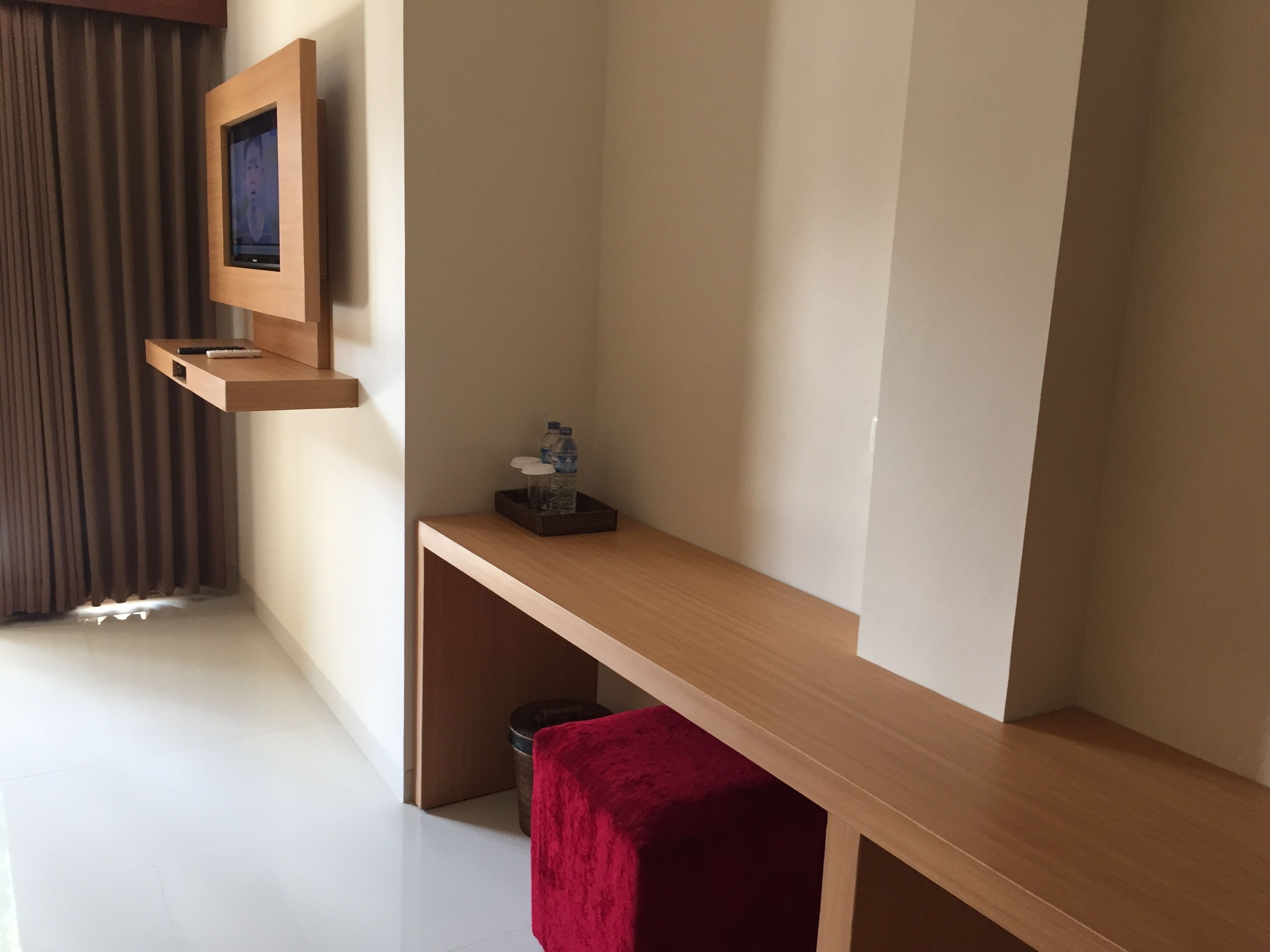 A modern hotel room with a wooden console table, a mounted television, and a red stool.
