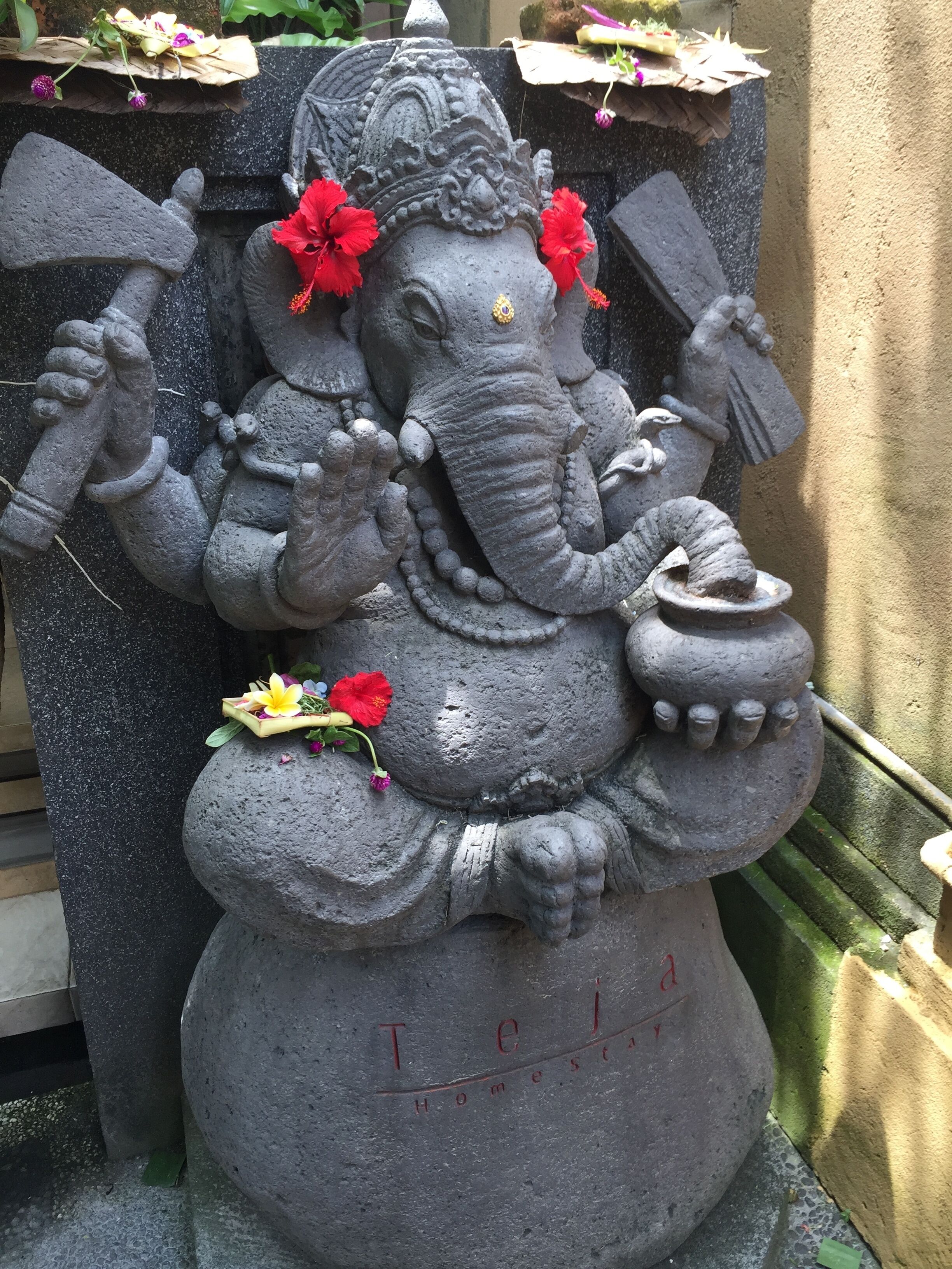 A stone statue of a deity with a hammer and a pot, surrounded by flowers.