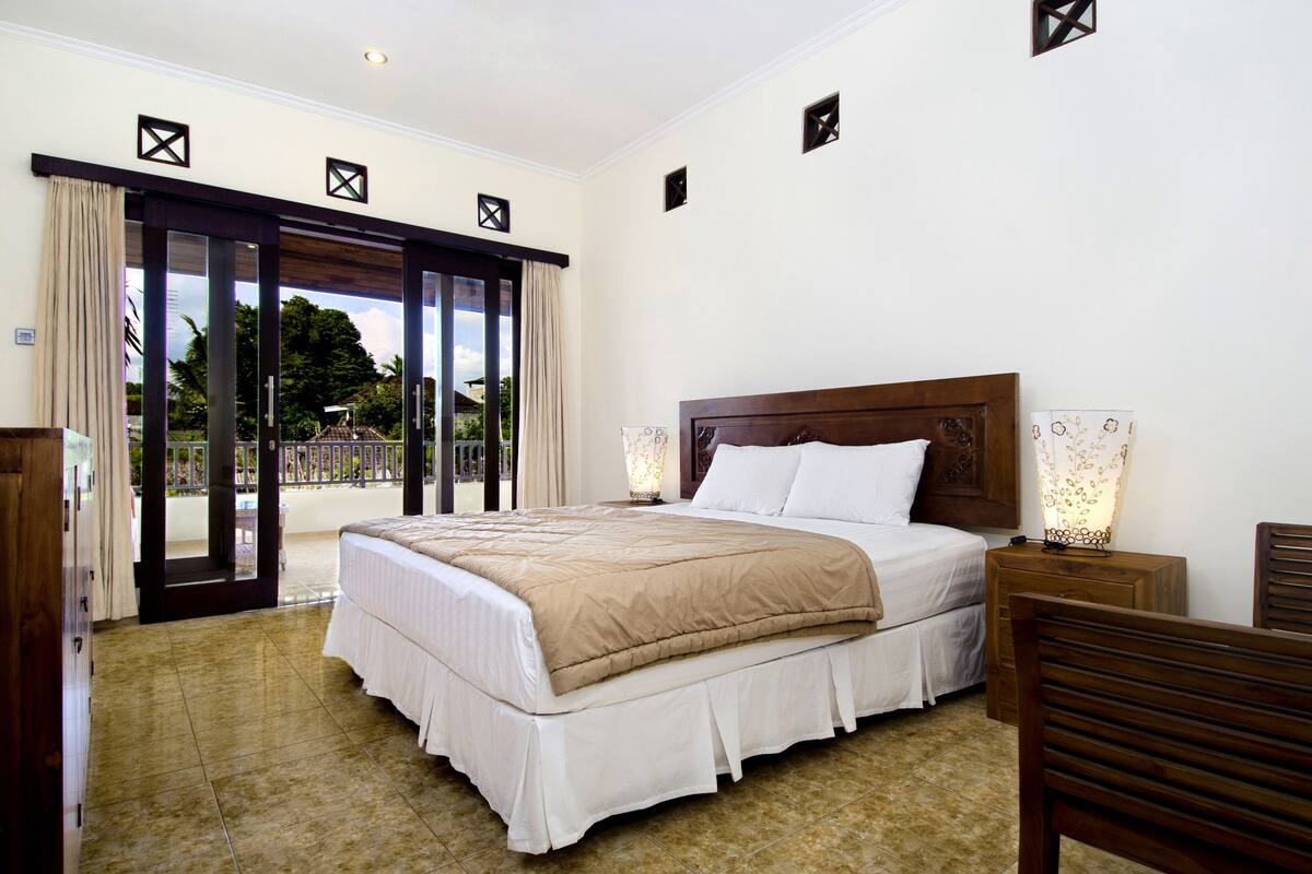 A spacious bedroom with a large bed, a wooden headboard, and a view of a balcony.