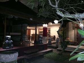 A traditional courtyard with stone statues, a wooden bench, and a tiled floor. - Teja Homestay (Ubud)