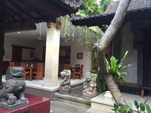 A traditional interior with stone lion statues, a wooden dining area, and hanging plants. - Teja Homestay (Ubud)