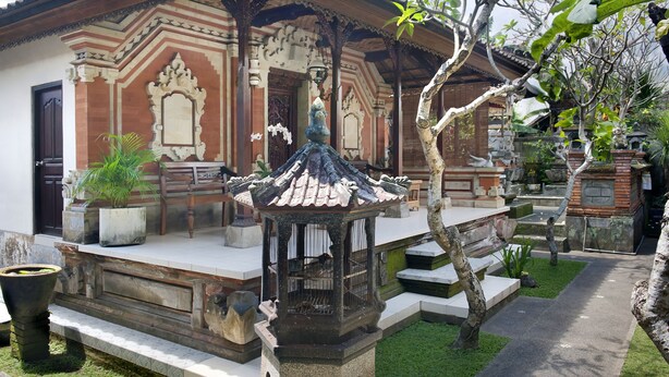 Edificio tradicional con tejado de azulejos y arquitectura ornamentada, rodeado de un jardín bien cuidado con una jaula de pájaros y plantas en macetas.