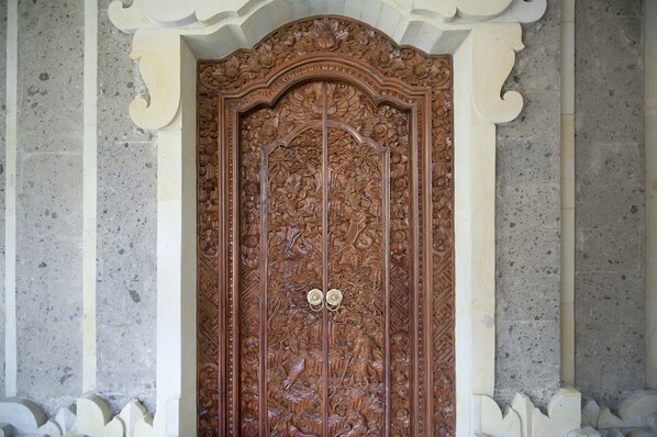 A detailed wooden door with intricate carvings, flanked by white columns with decorative capitals. - Teja Homestay (Ubud)