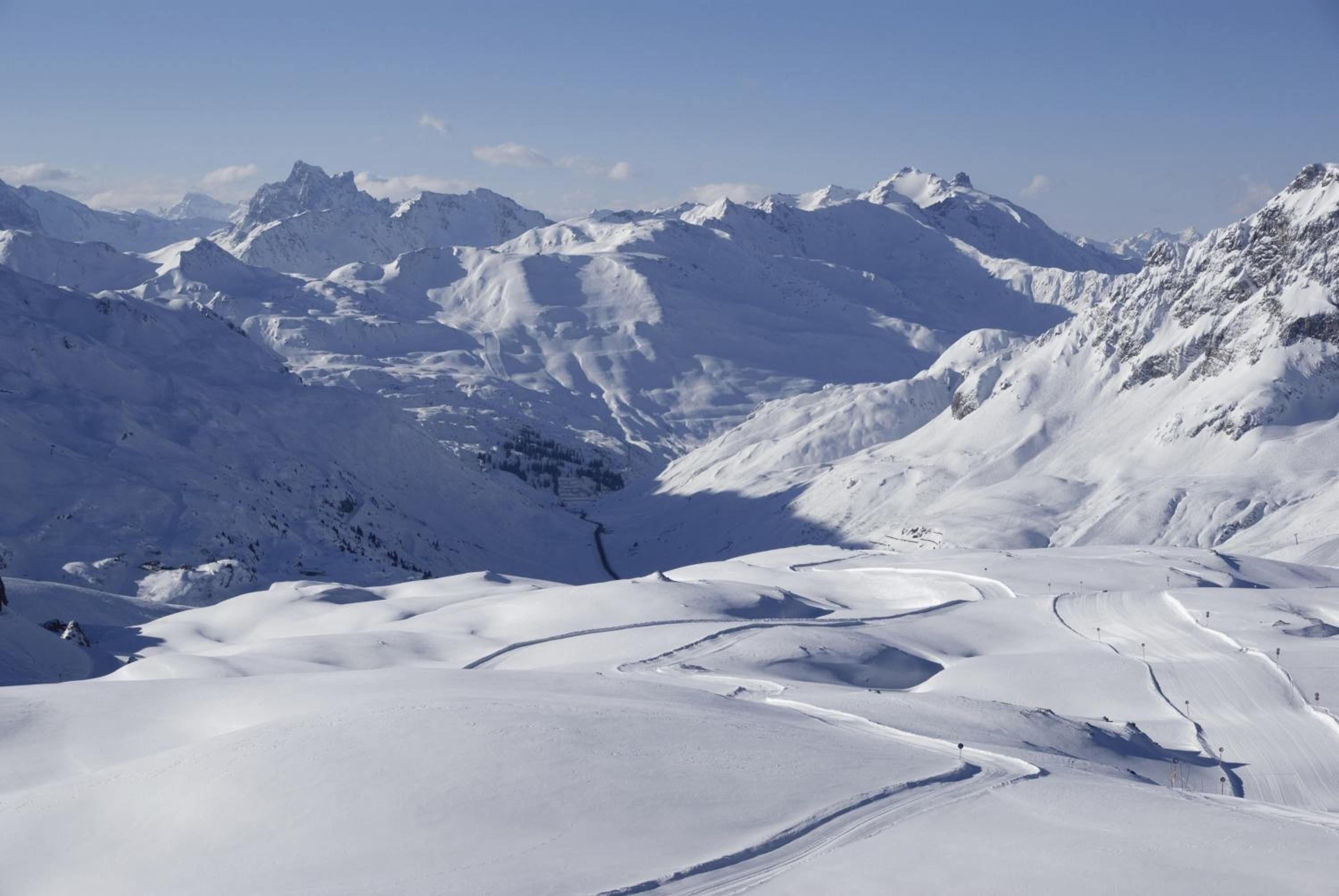 A snow-covered mountainous landscape with winding trails and a clear sky.