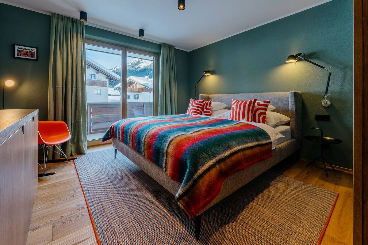 Una moderna camera da letto con un letto grande, una scrivania e una sedia. Si vede una vista sulle montagne dalla finestra.