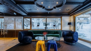 A modern living room with a green sofa, two dark armchairs, a glass coffee table, and colorful stools. - Appart Hotel Knappaboda (Lech am Arlberg)