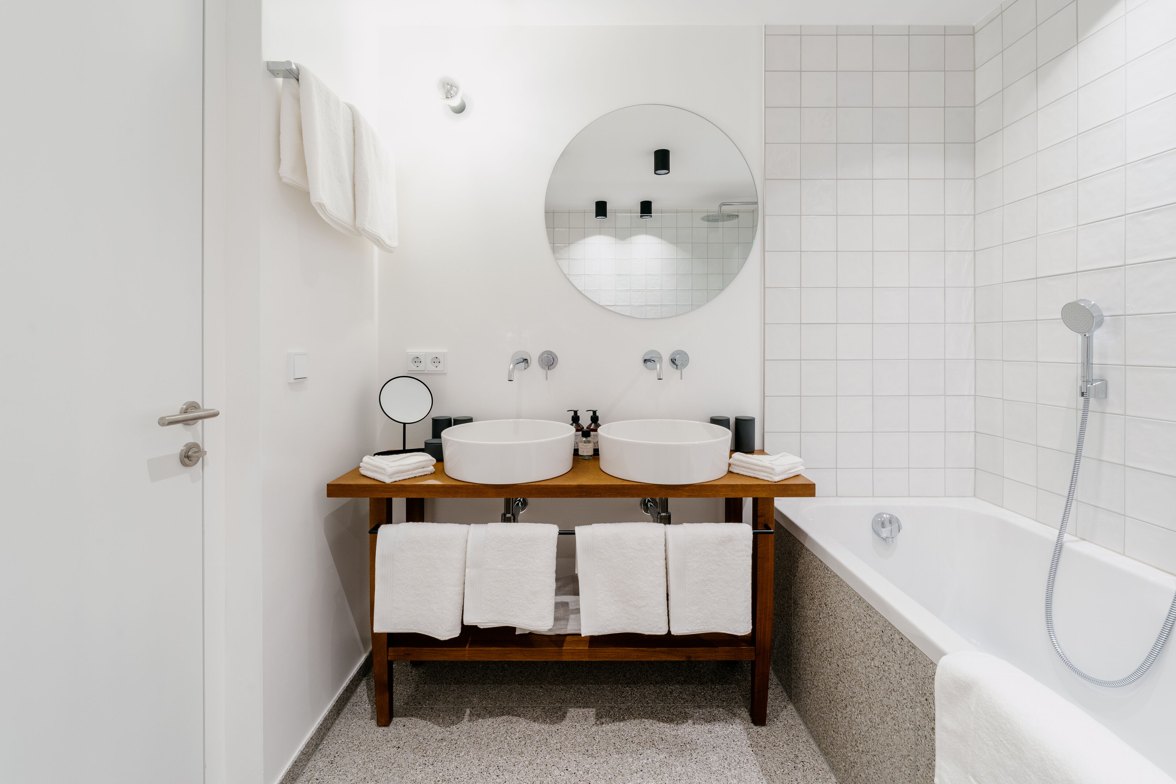 A modern bathroom with two sinks, a round mirror, a bathtub, and a shower.