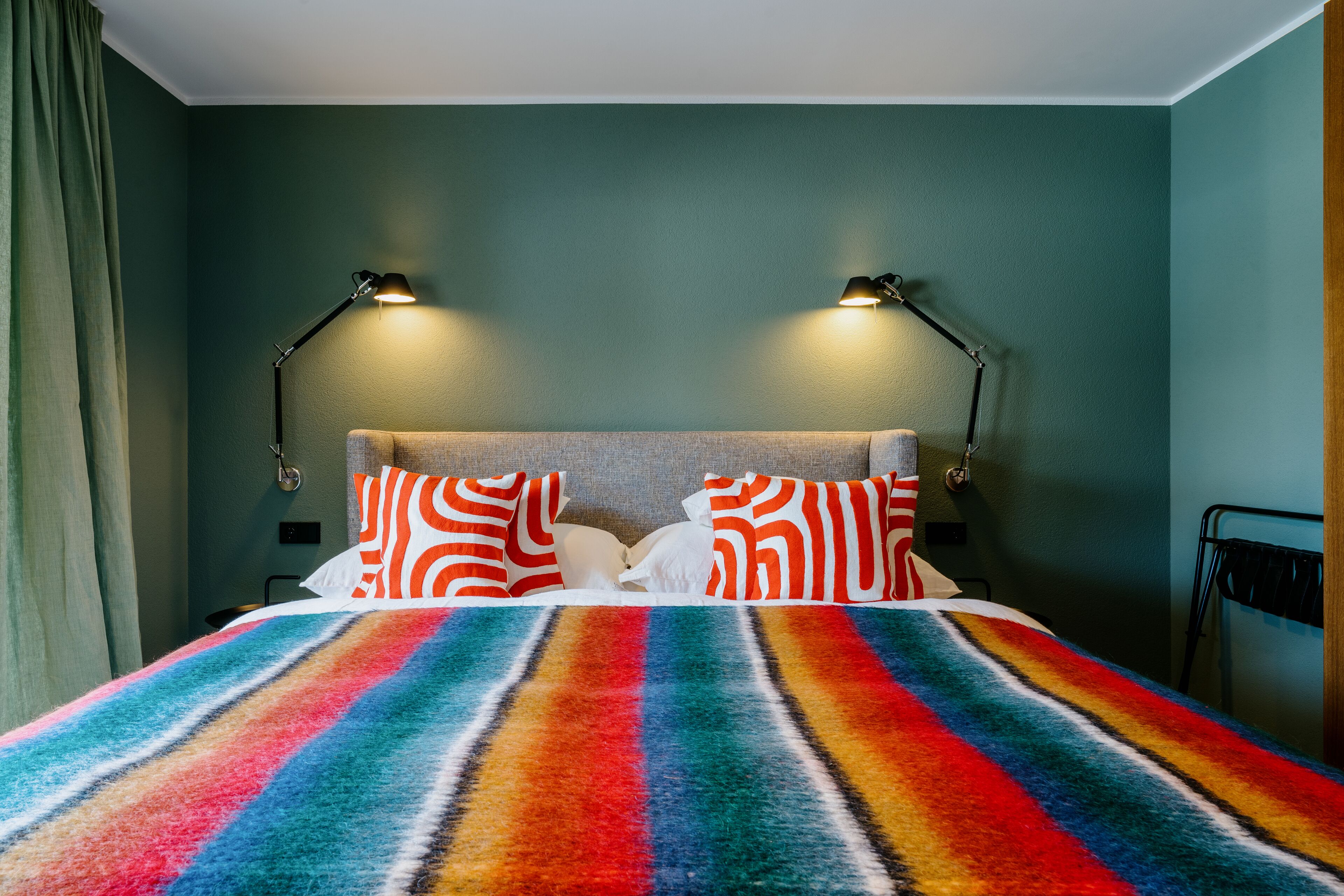 A bed with a colorful striped blanket, two lamps, and patterned pillows.