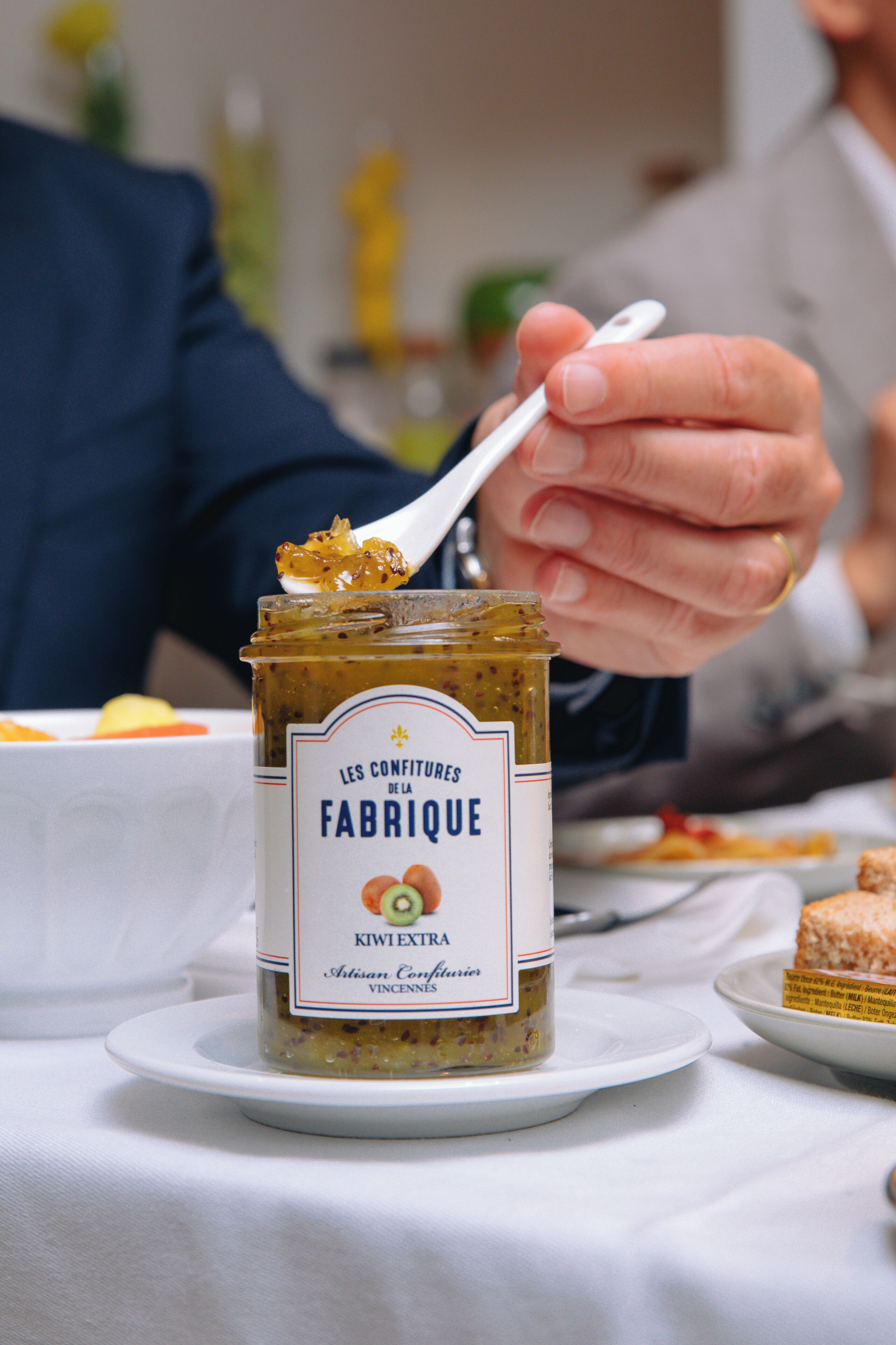 A jar of kiwi jam on a white plate with a spoonful being lifted.