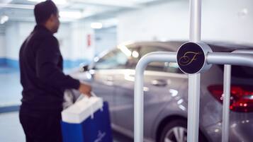 Un parking avec une voiture et une personne tenant une boîte bleue.