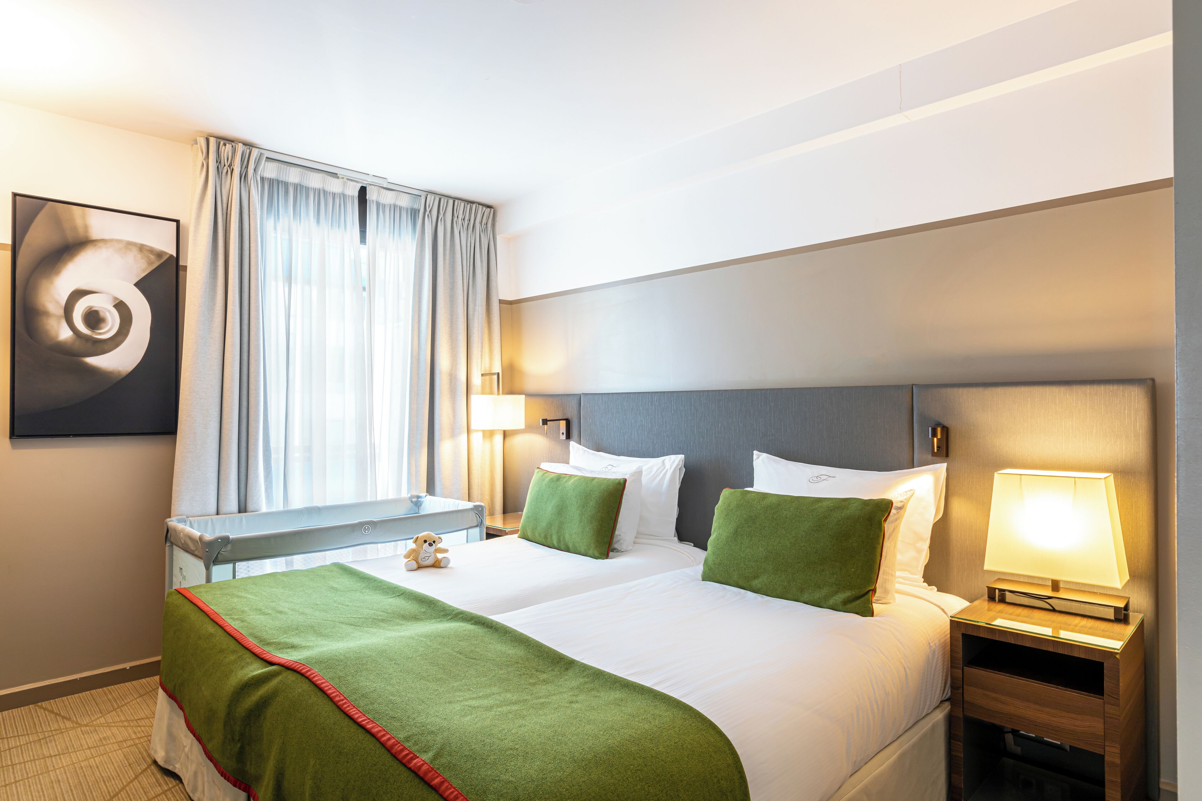 A hotel room with a large bed, two bedside tables, a desk, and a window with curtains.