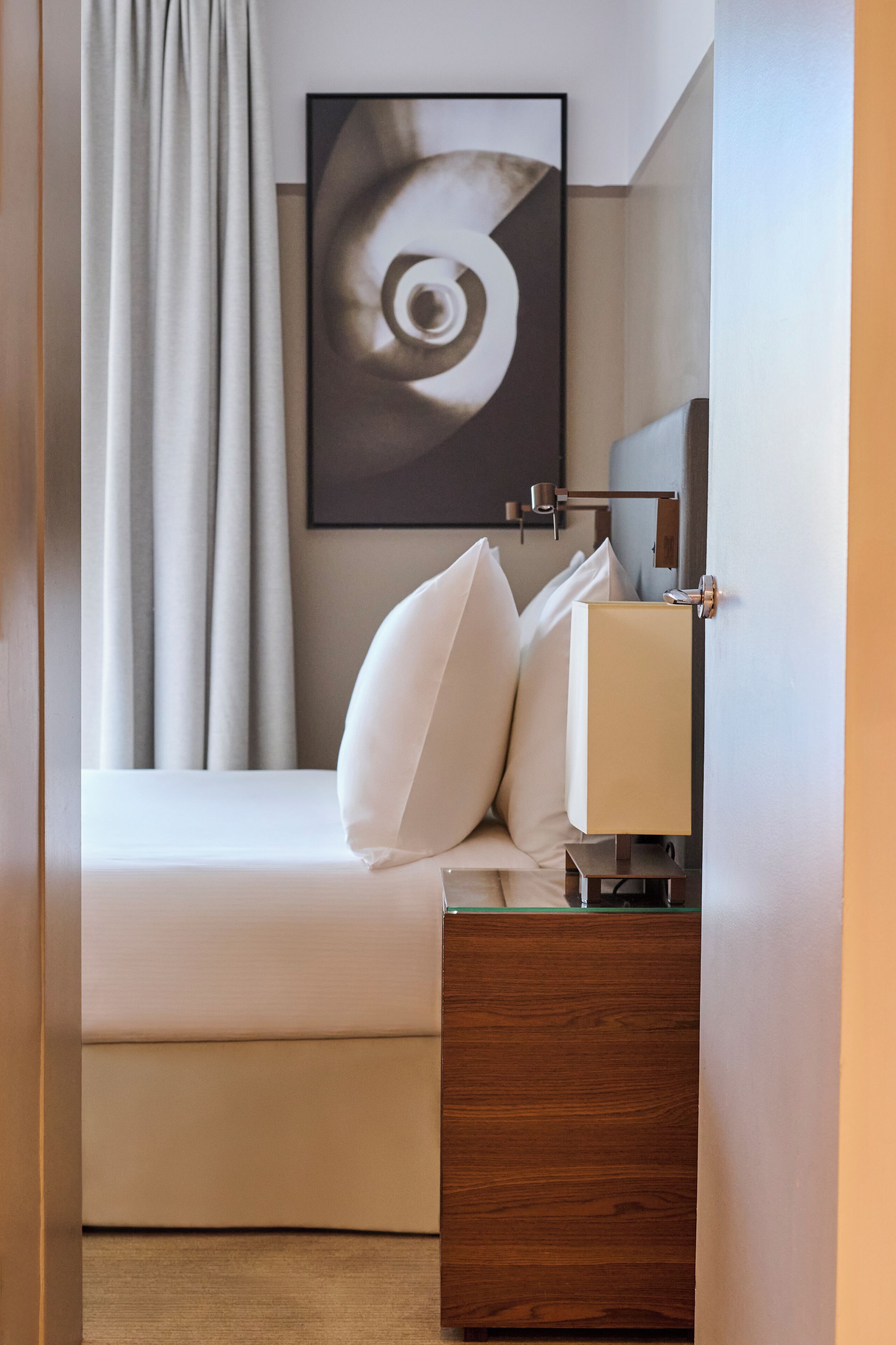 Habitación de hotel ordenada con cama, mesita de noche, lámpara y un cuadro en la pared.