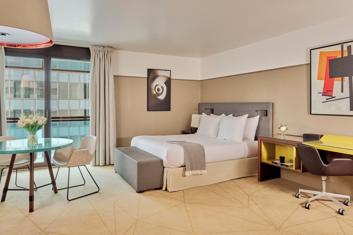 Ein Hotelzimmer mit Bett, Schreibtisch, Stuhl, kleinem Tisch und einer Vase mit Blumen.