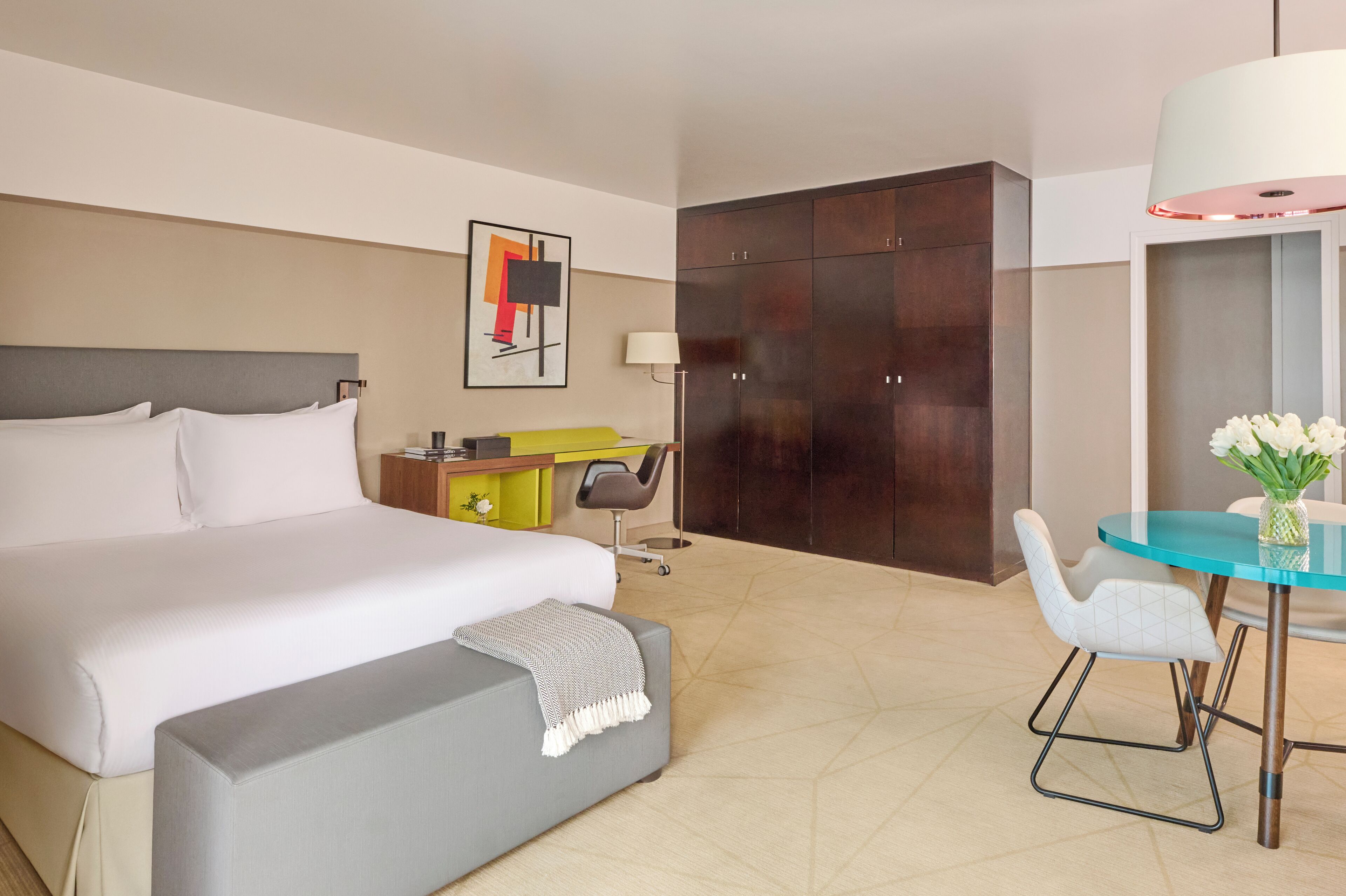 Ein Hotelzimmer mit einem großen Bett, einem Schreibtisch mit Stuhl, einem Kleiderschrank und einem Esstisch mit Stühlen.