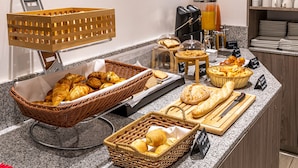 A breakfast buffet with various breads, pastries, and a coffee station.