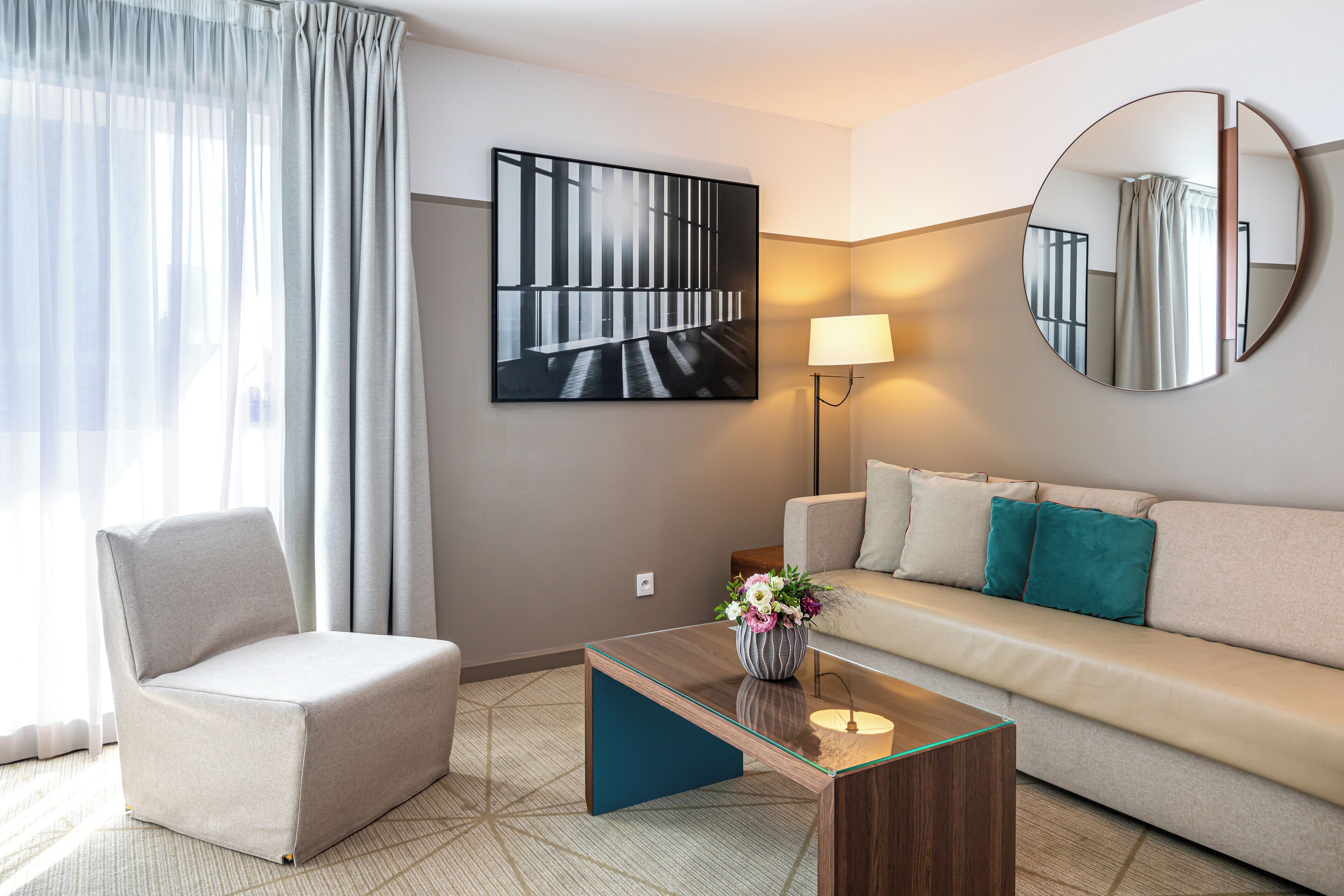 Quarto de hotel moderno com sofá, poltrona e mesa de centro de vidro.