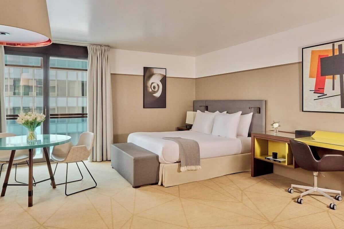 Ein Hotelzimmer mit einem Bett, einem Schreibtisch, einem Sessel, einem kleinen Tisch und einem Fenster mit Vorhängen.