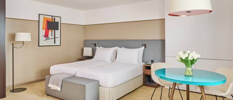 A hotel room with a bed, bedside table, lamp, and a round table with a vase of flowers.