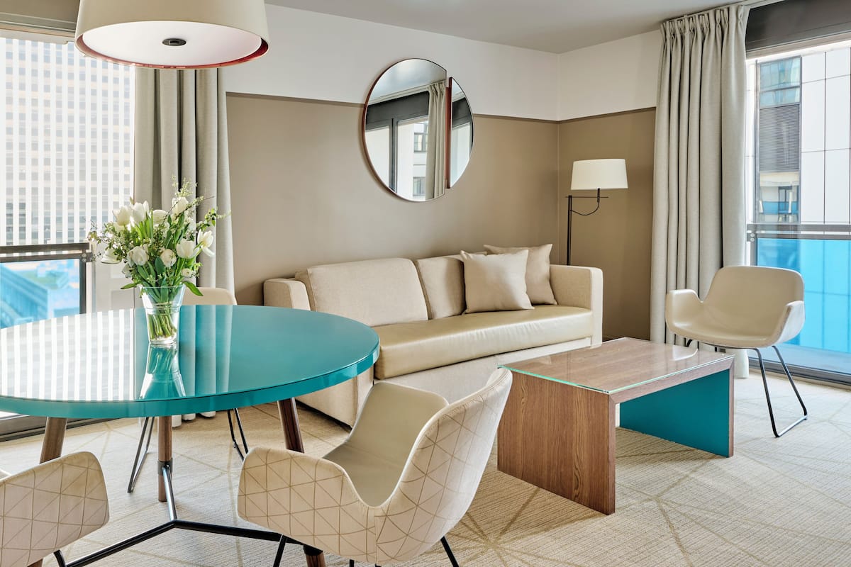 Ein modernes Hotelzimmer mit rundem Glastisch, beiger Couch und einem einzelnen Sessel.