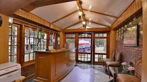 A reception area with a wooden counter, a printer, and a view of the outdoor patio through glass doors. - The Woodstock Resort (Shimla)