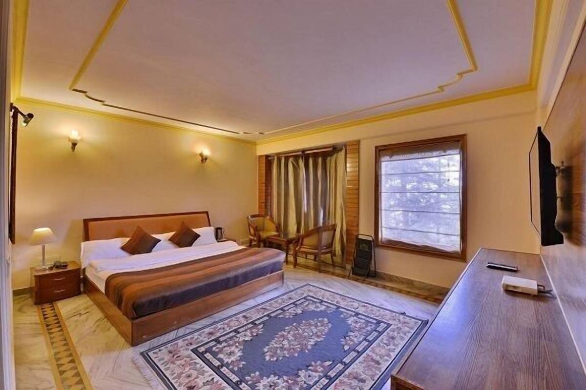 Ein Schlafzimmer mit einem großen Bett, einem Schreibtisch, einem Stuhl, einer Lampe und einem Fenster mit Vorhängen.