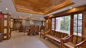 A spacious room with a wooden ceiling, a dining area with chairs and a table, and a large window with a view of trees. - The Woodstock Resort (Shimla)