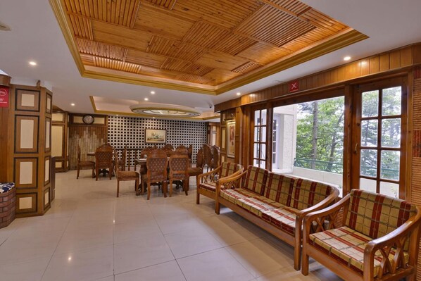 A spacious room with a wooden ceiling, a dining area with chairs and a table, and a large window with a view of trees.