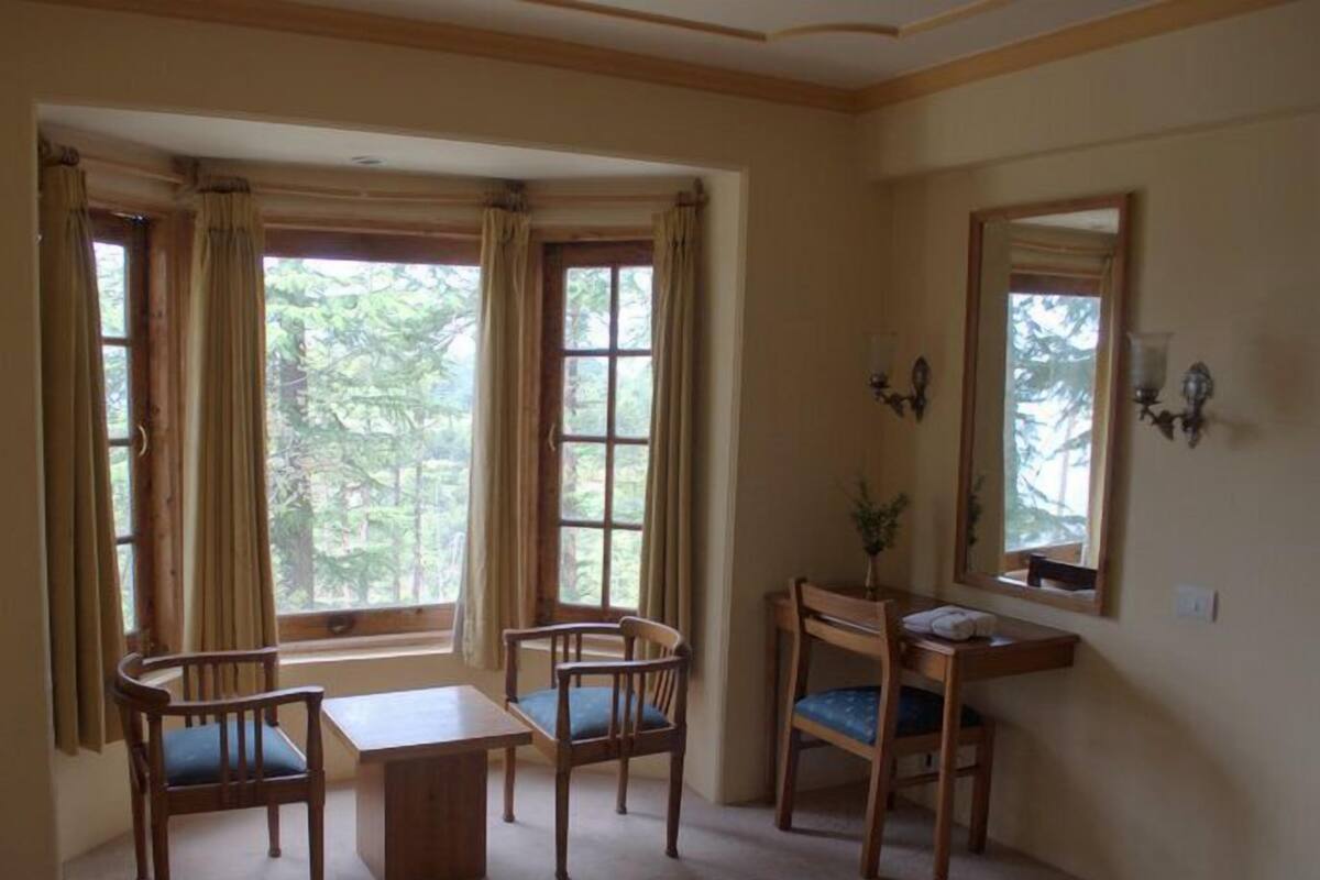 Ein Zimmer mit einem großen Fenster, zwei Stühlen, einem kleinen Tisch und einem Spiegel an der Wand.