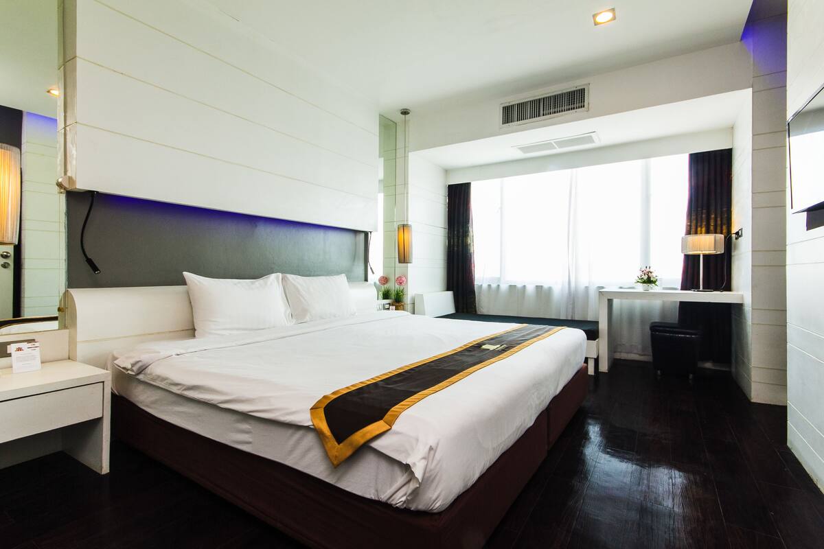 A hotel room with a large bed, a desk, and a window with curtains.