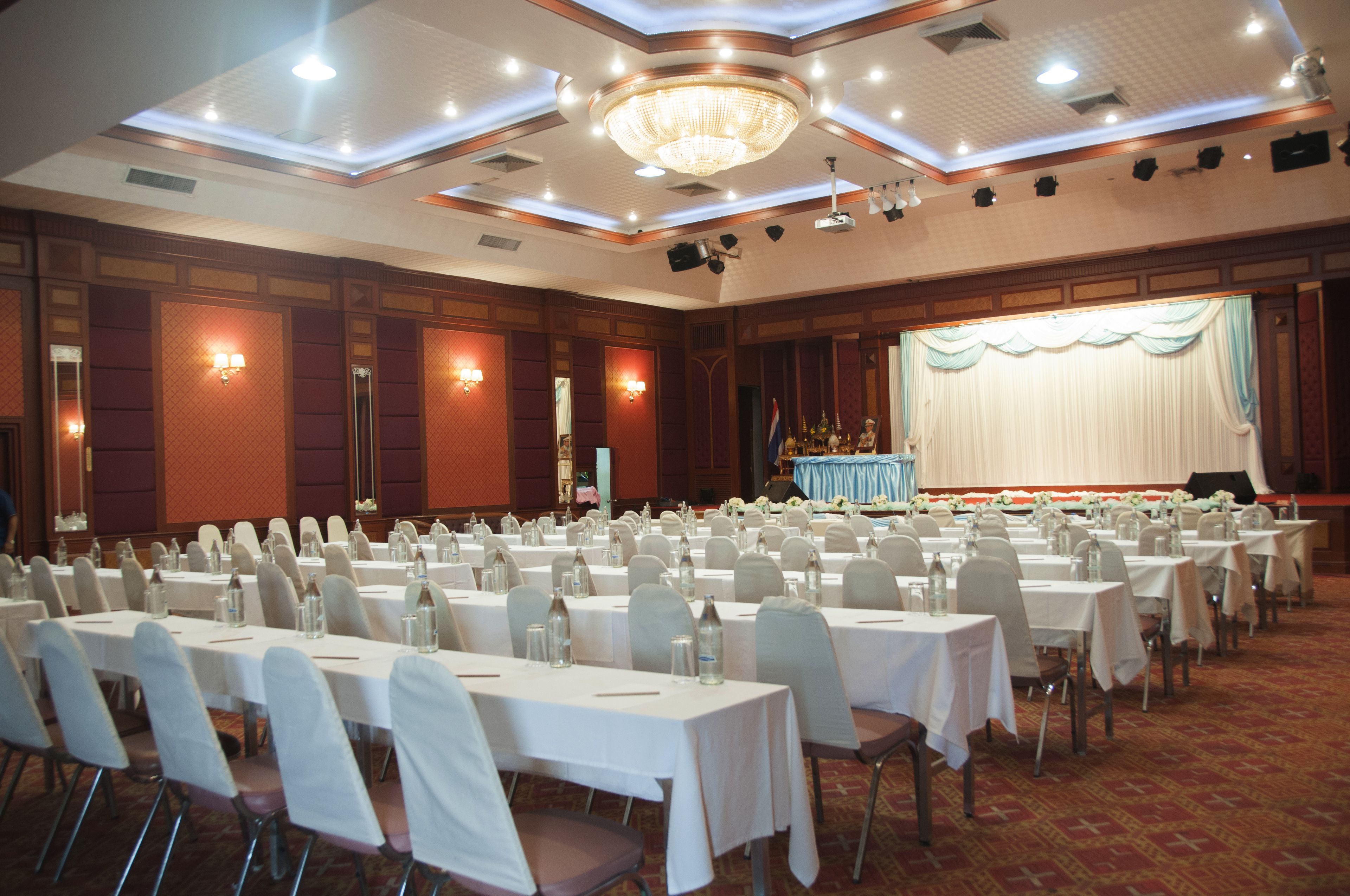 Uma sala de banquetes com fileiras de mesas, cadeiras e um palco com um pano de fundo.