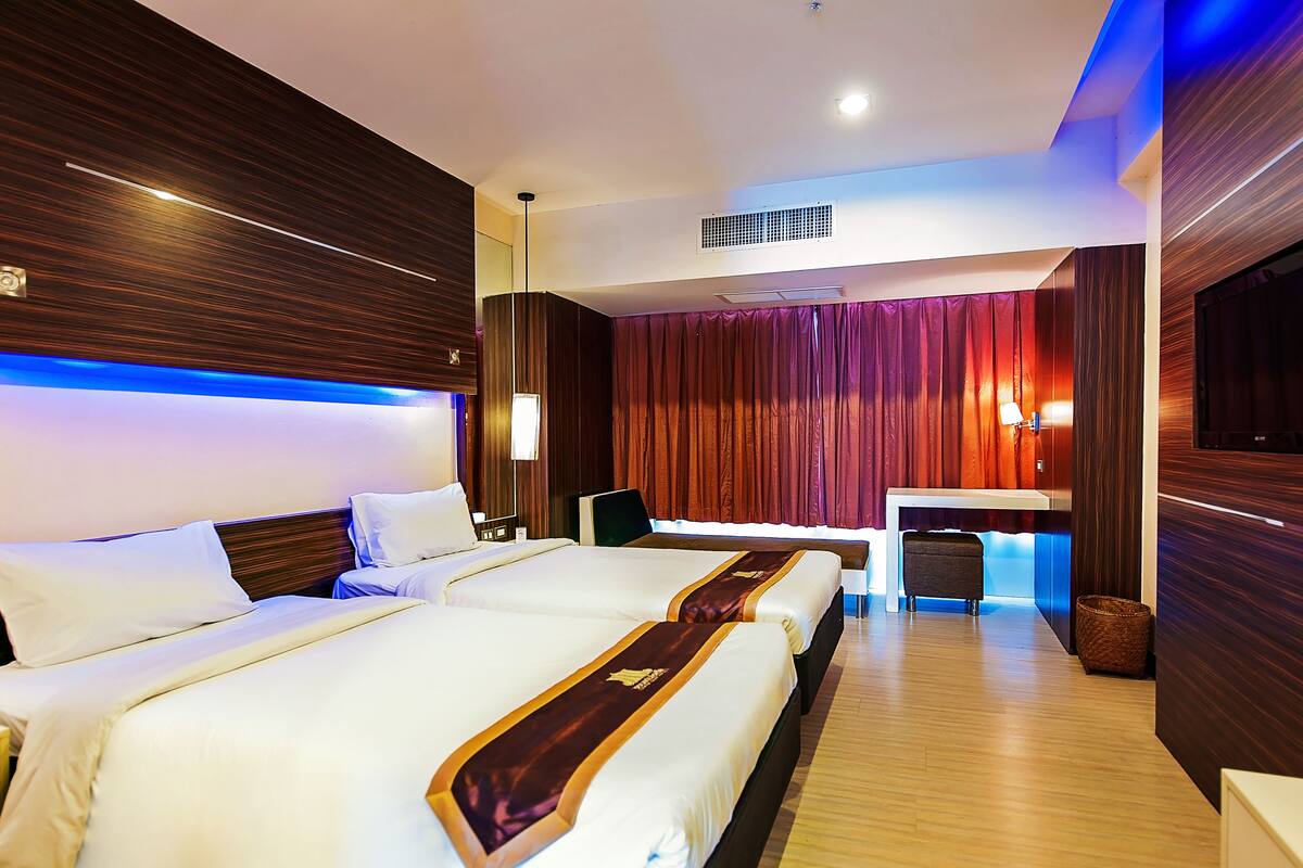A hotel room with two beds, a desk, a chair, and a TV.