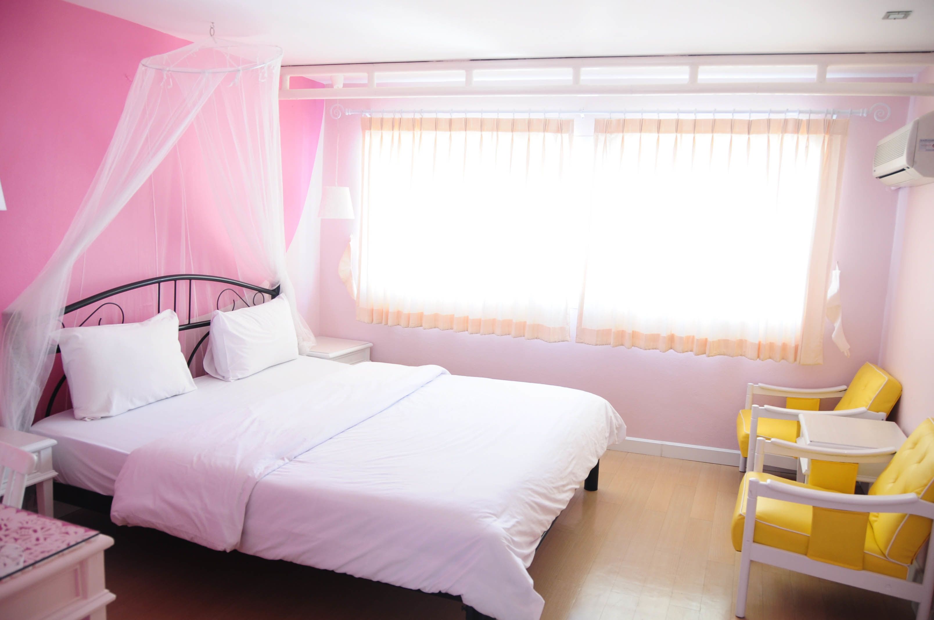 A bedroom with a bed, a nightstand, a chair, and a window with curtains.