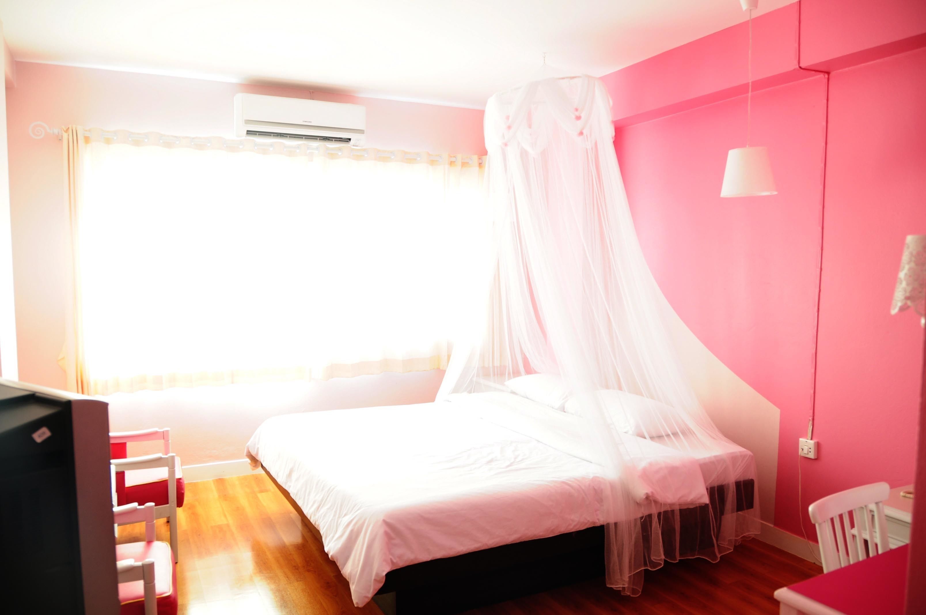 A bedroom with a bed, a chair, a desk, and an air conditioning unit.