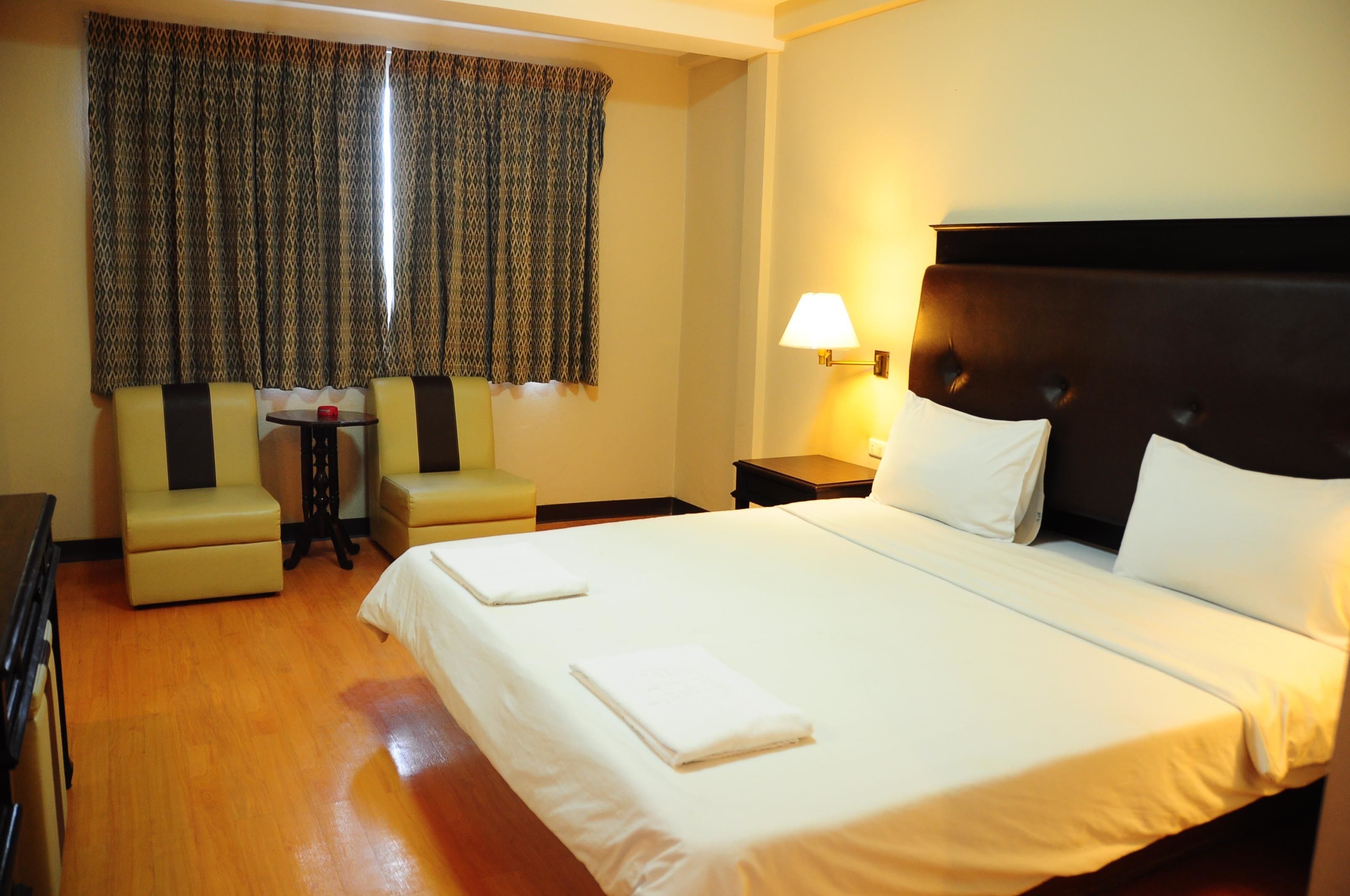 Une chambre d’hôtel avec un grand lit, deux fauteuils, une petite table et une lampe.