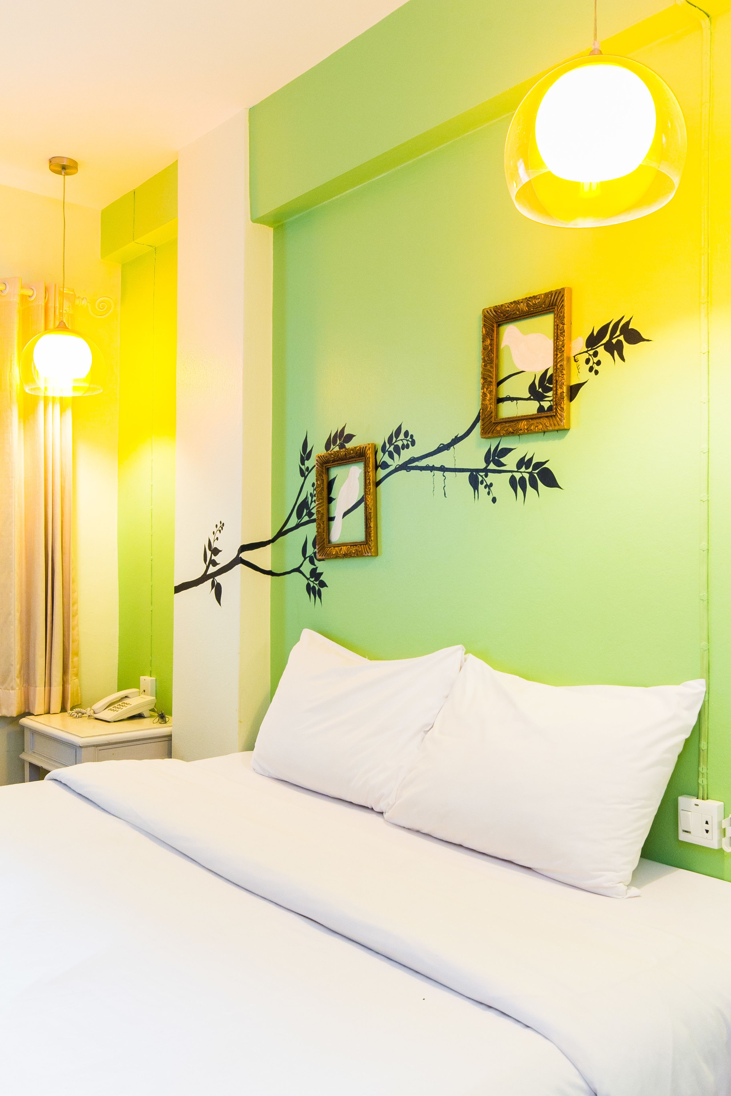 A hotel room with a bed, a nightstand, a telephone, and a wall with a branch design and two framed pictures.