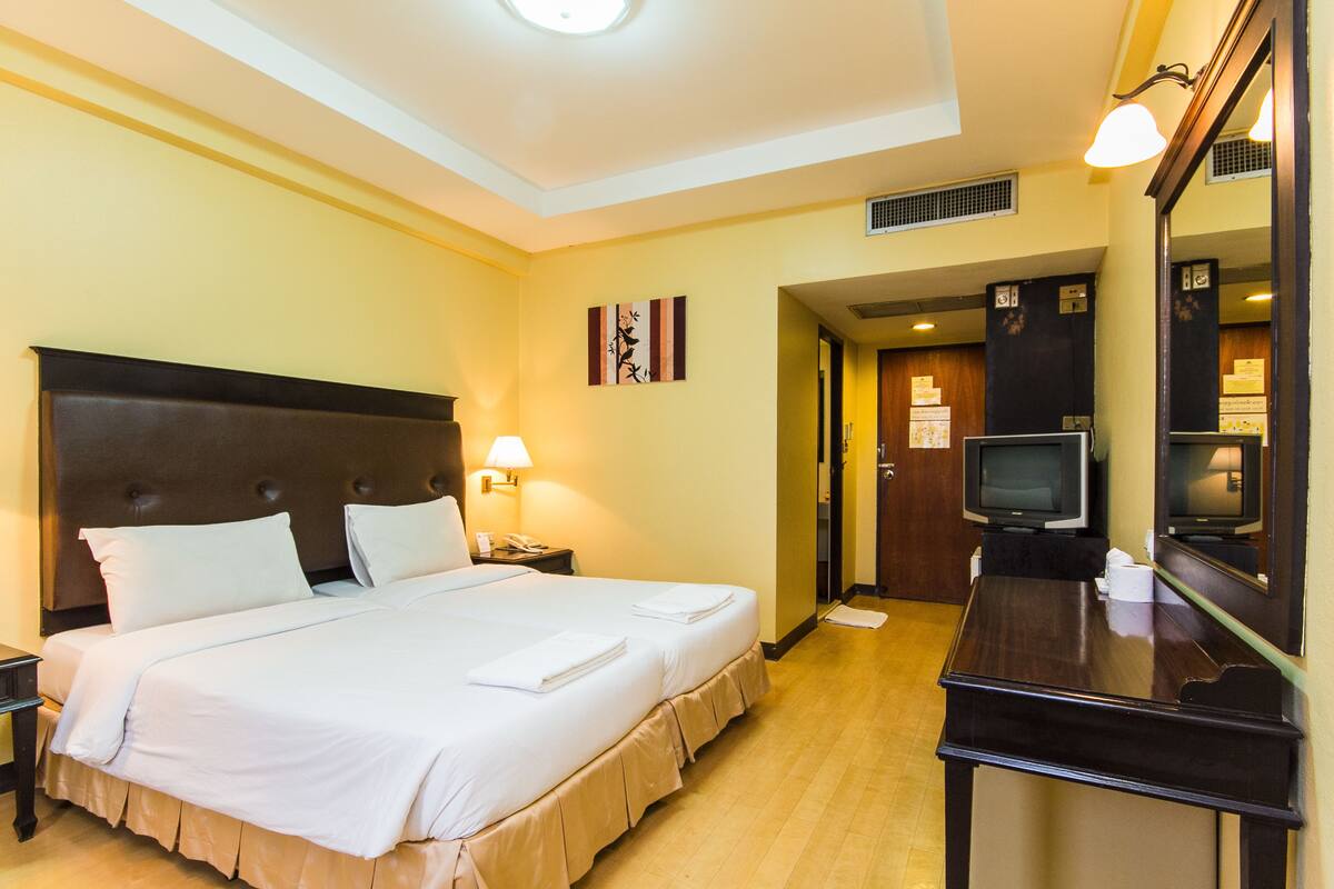 A hotel room with a large bed, bedside tables, a desk with a mirror, a television, and a door leading to a bathroom.
