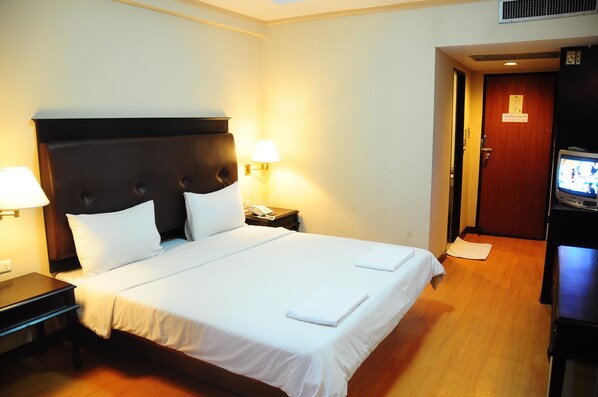 A hotel room with a large bed, two bedside lamps, a TV, and a wooden floor.