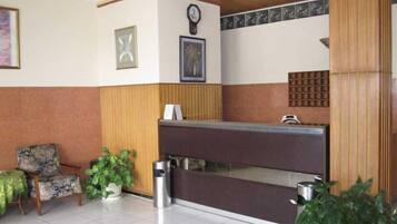 A reception area with a wooden reception desk, a clock, framed artwork, and potted plants.