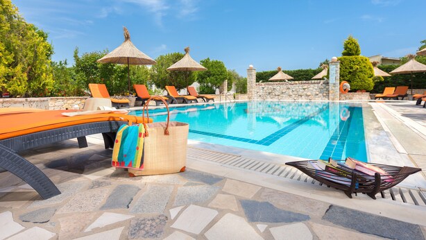 Zona de piscina con sillones de descanso, sombrillas y un muro de piedra.