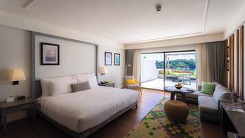 A hotel room with a large bed, a sofa, a dining table, and a view of the outdoors.