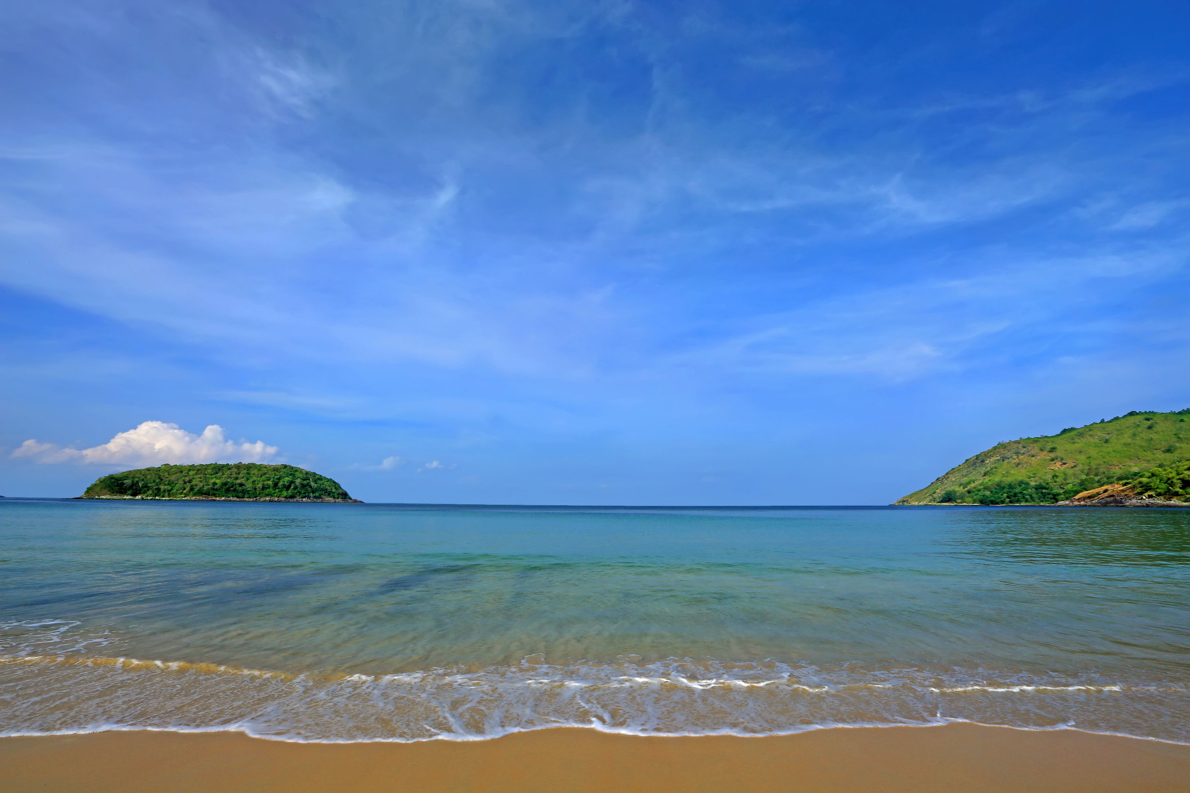 A beach with clear water, a sandy shore, and a small island in the distance.