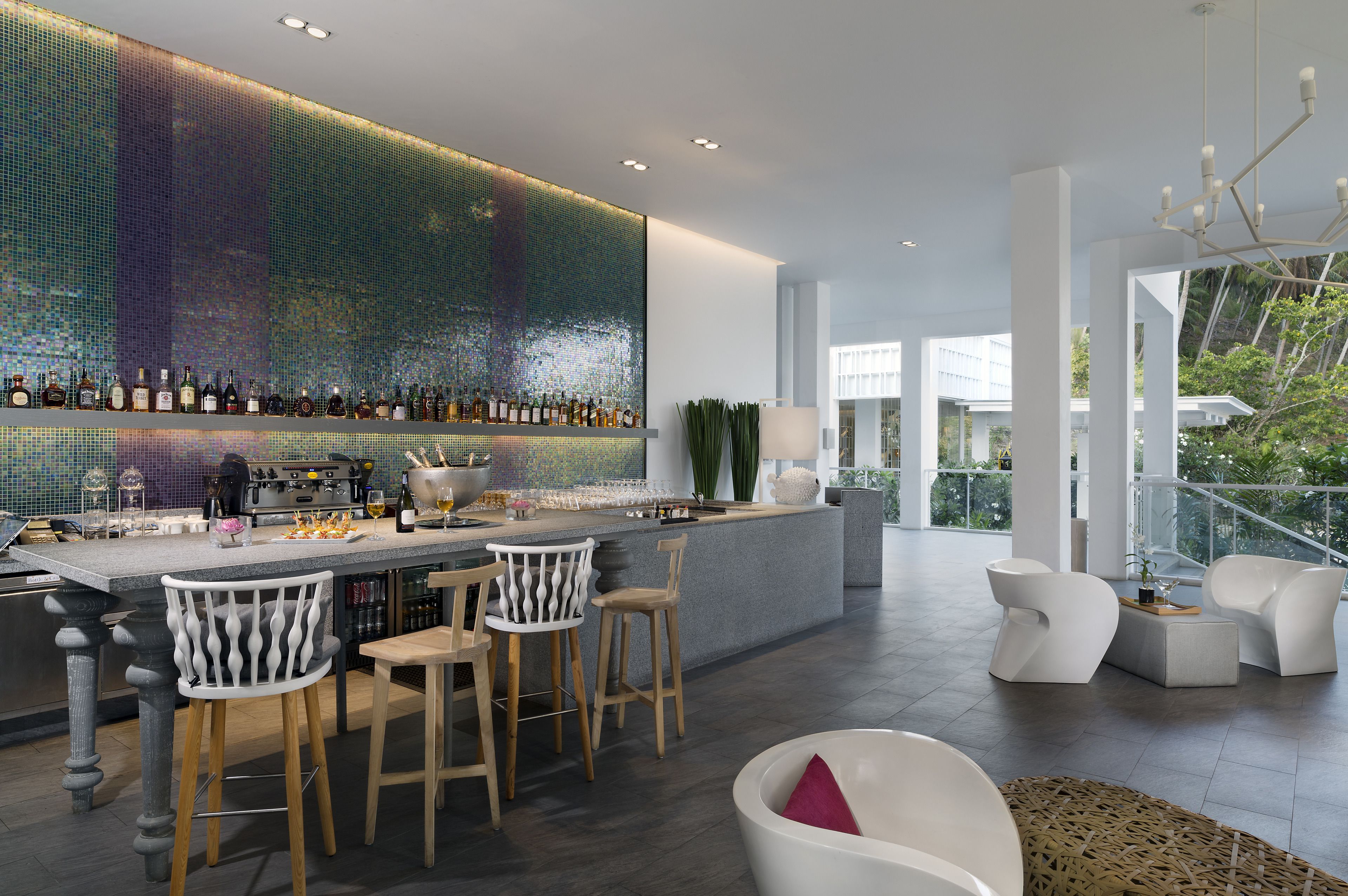 Un bar moderno con un revoque de mosaico, taburetes y una zona de estar con sillas blancas.