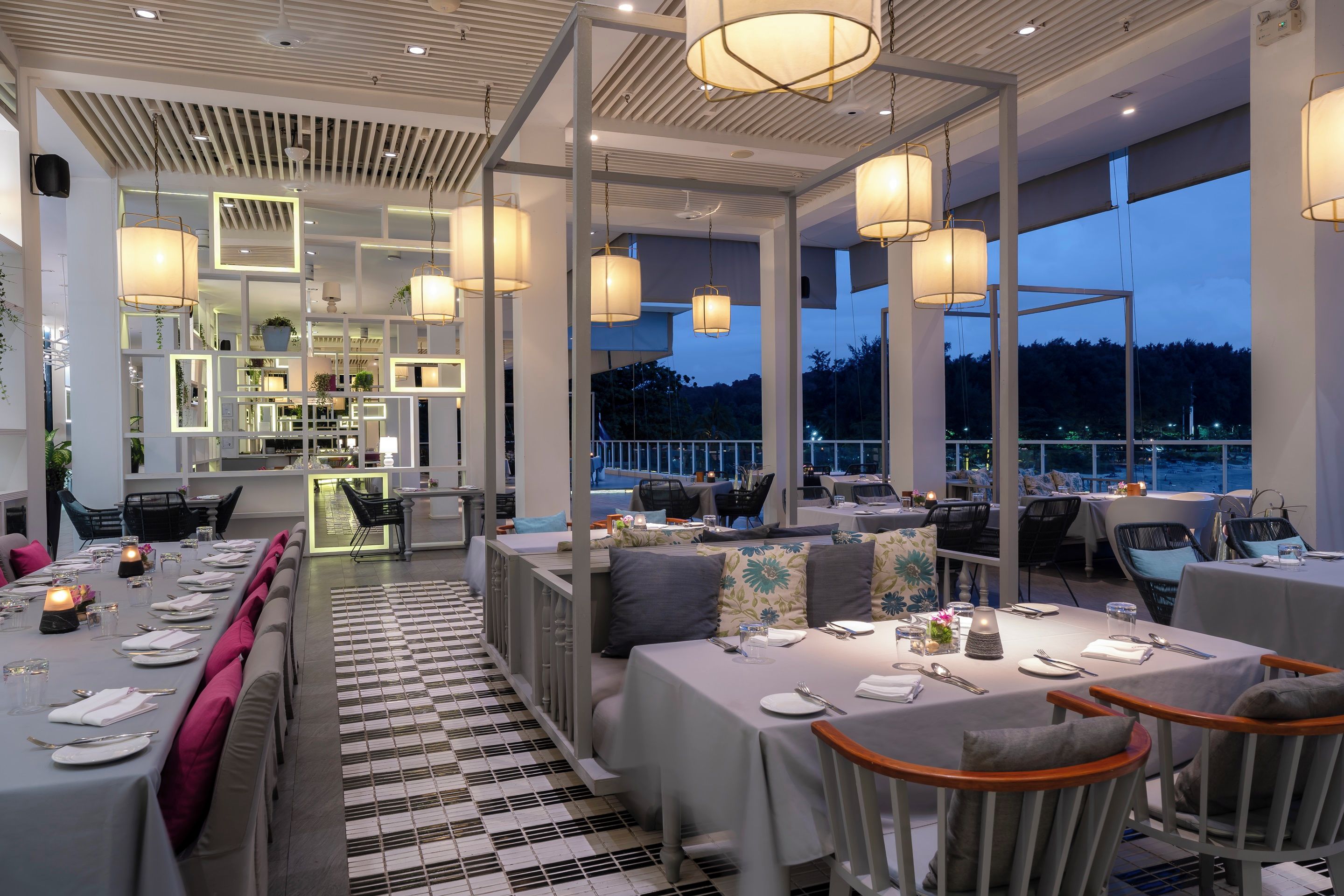 A modern restaurant with high ceilings, pendant lighting, and a checkered floor. Tables are set for dining with chairs.
