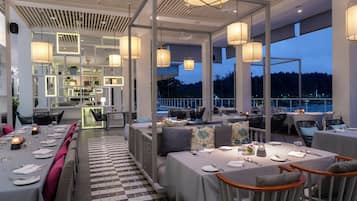 A modern restaurant with high ceilings, pendant lighting, and a checkered floor. Tables are set for dining with chairs.