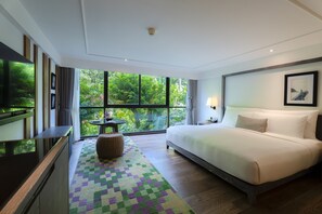 Relax in a spacious room with a large bed, flat-screen TV, and a small table with a lamp.